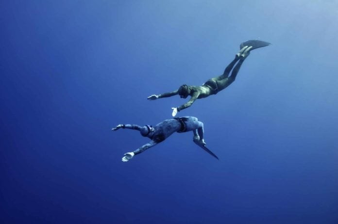Two freedivers - the man and the woman - are making the simultaneous dive at the depth of Blue Hole, Red Sea, Egypt. The picture seems very romantic.