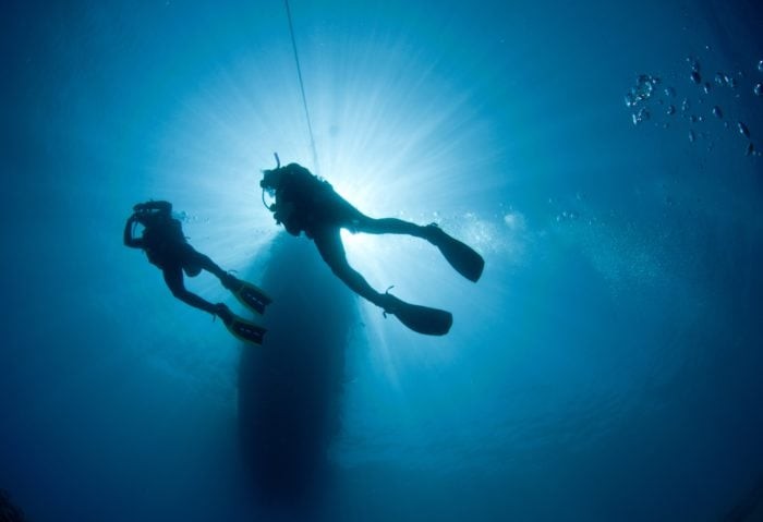 Two scuba divers are silhouetted in blue water