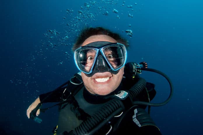 Smile of crazy Scuba diver underwater selfie in the deep blue ocean and backlight sun