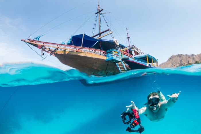 A freediver swims underwater next to a traditional boat on a tropical coral reef
