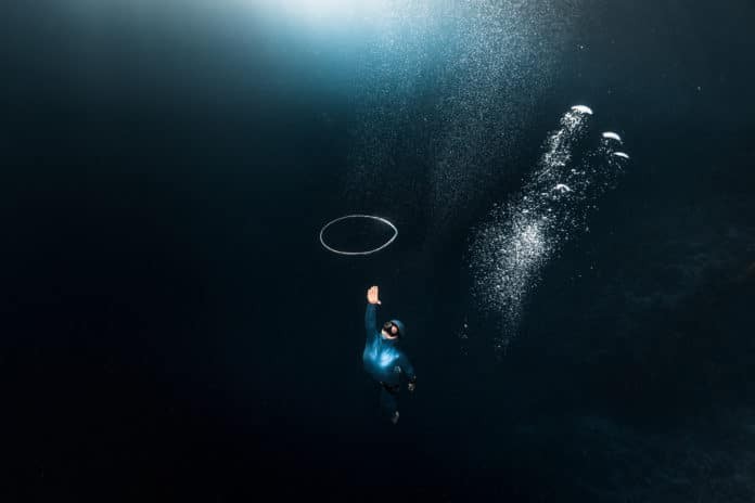 Woman free diver chases bubble ring rising from the depth