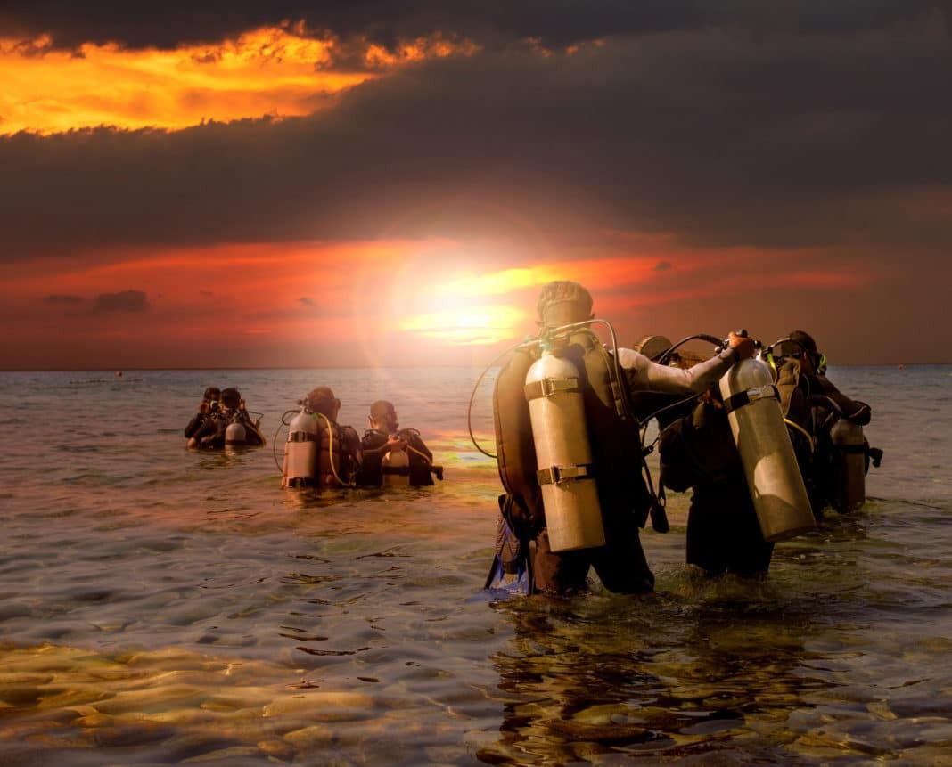 group of scuba diving preparing to night diving at sea side against beautiful sun set sky