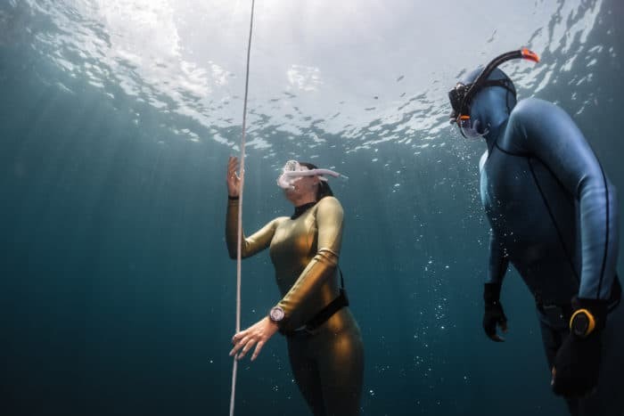 Two lady free diver ascending along the rope in the depth