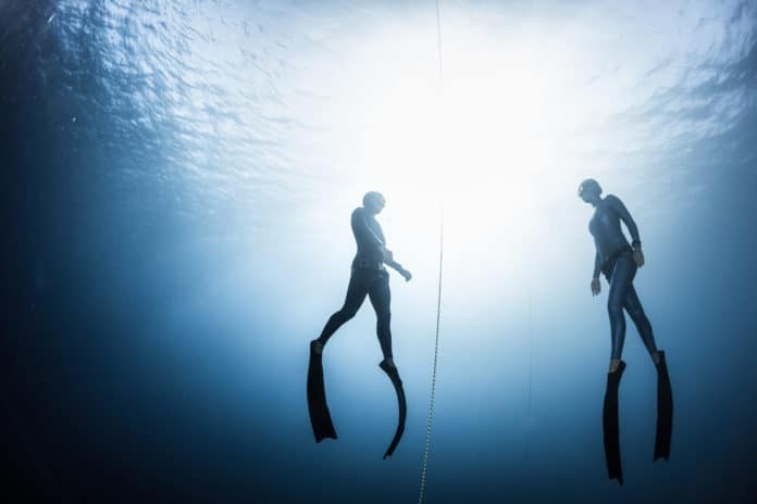 Two freedivers, man and woman, ascending from the depth