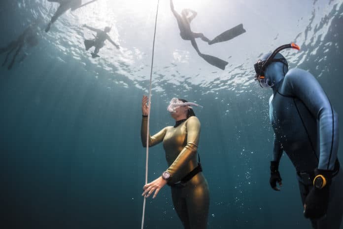 Lady free diver ascending along the rope in the depth