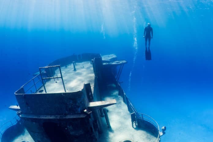 Freedivers swimming through a large underwater shipwreck