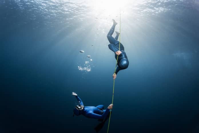 Two freedivers play with bubbles near the rope