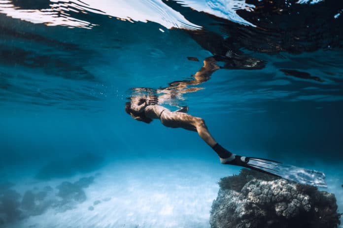Woman freediver relax over sandy sea with fins. Underwater in blue ocean