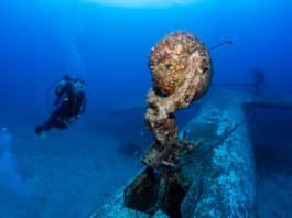 Scuba Diver explores the growth-encrusted landing gear of an underwater aircraft wreck