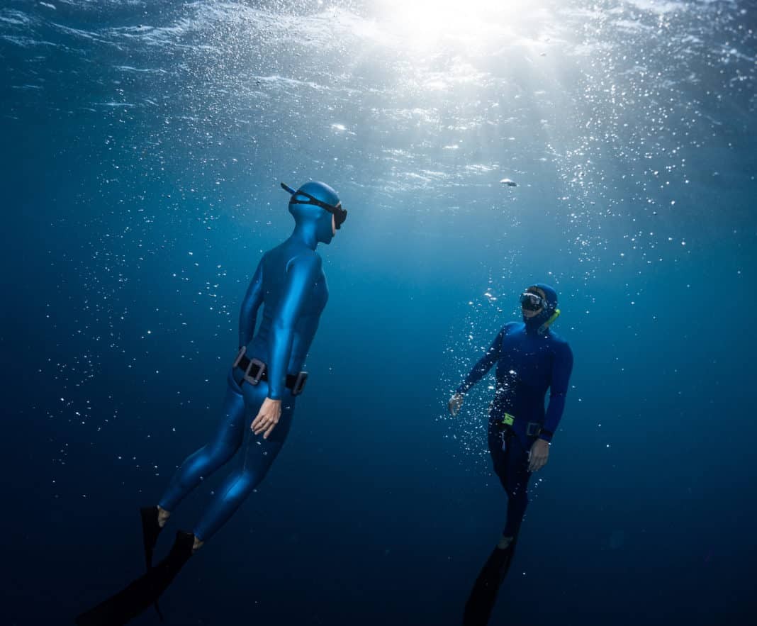 Two freedivers ascending surrounded by bubbles