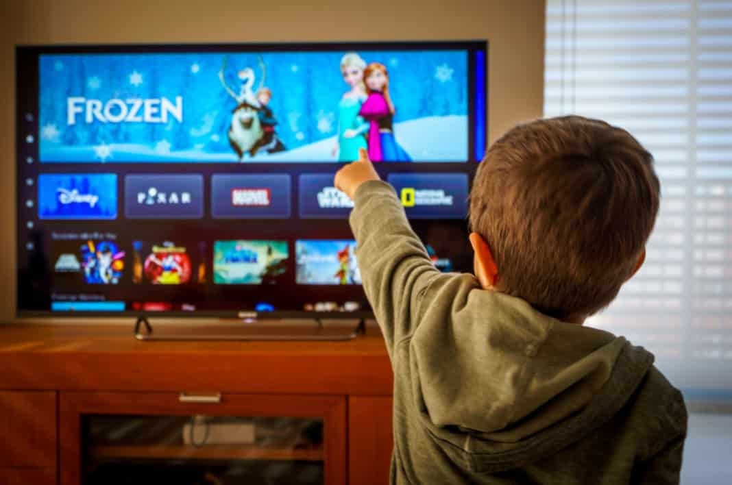 Little boy watching the new Disney plus streaming service and pointing at the TV screen.