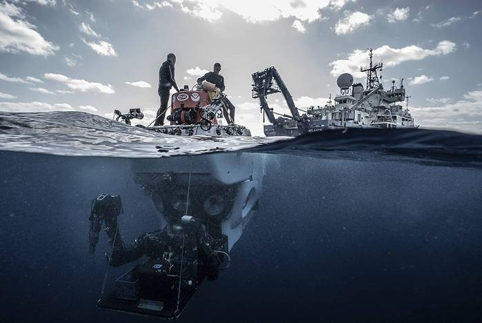Alvin team members stand atop HOV Alvin at the ocean’s surface after a dive in 2018, soon to return on-board R/V Atlantis in the distance. (Image credit: Luis Lamar/Woods Hole Oceanographic Institution)