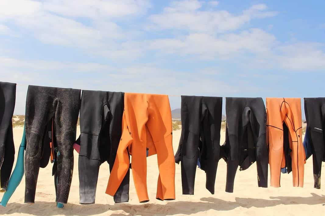 Colorful neoprene scuba diving wetsuits hanging on a rope to dry in the sun at the beach (Adobe Stock)